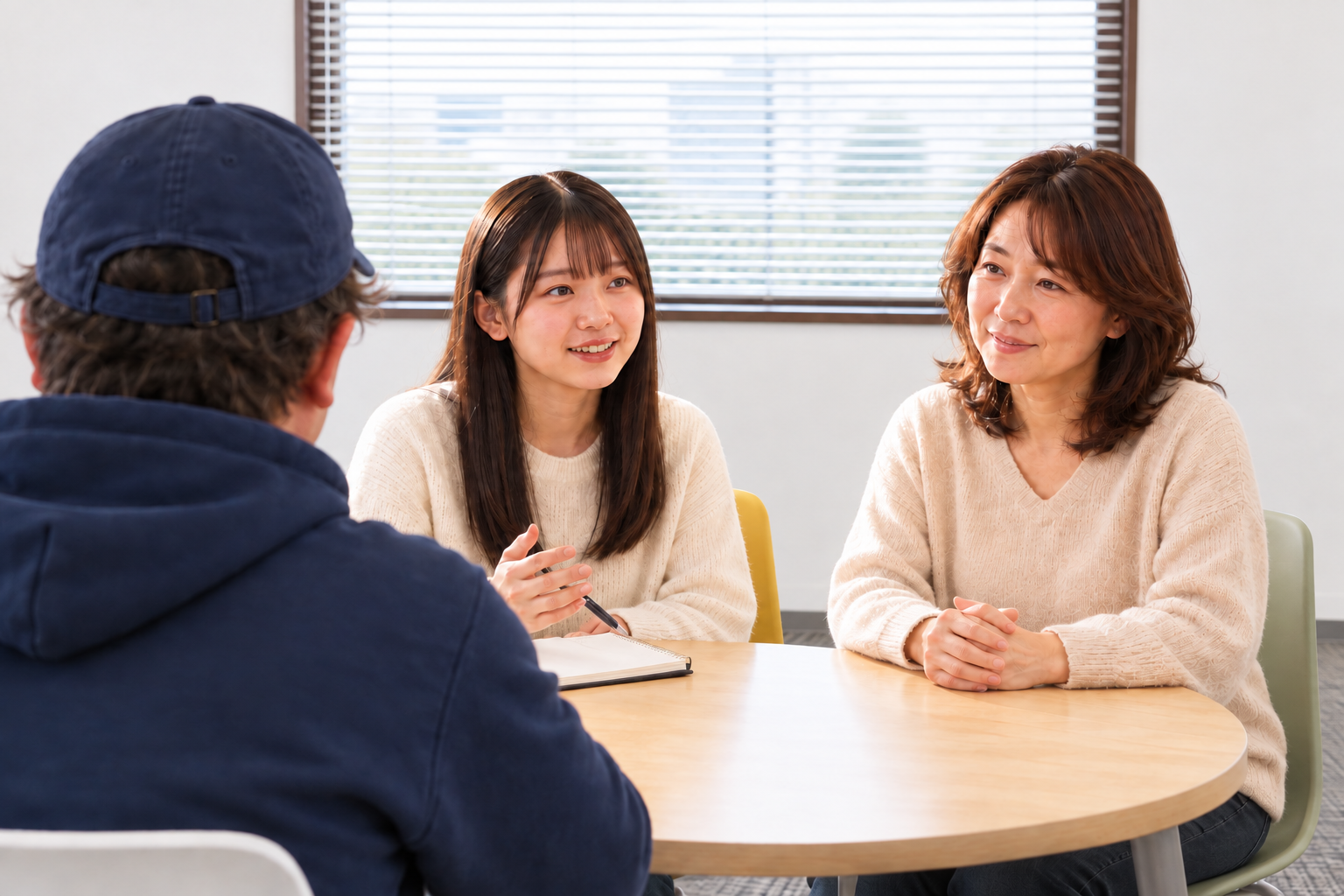 小さな教室の丸い机で、左手前の須藤と受験生の女の子・母親が相談しているイメージ